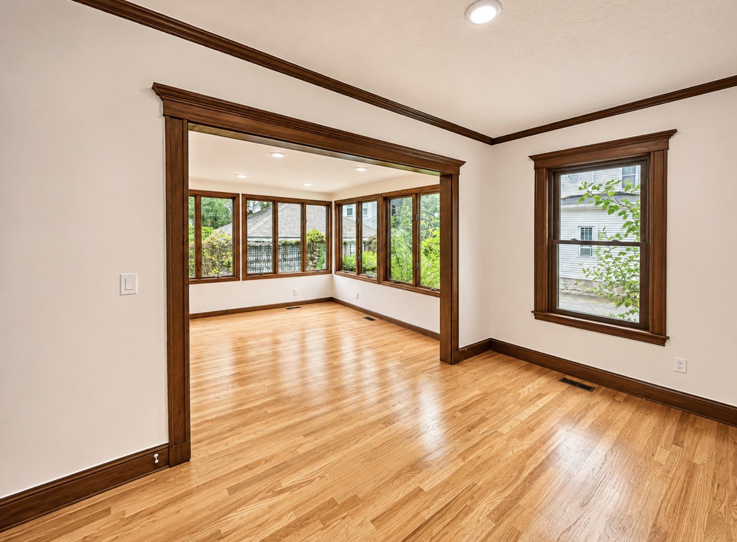 Room with white walls and dark stained trim opening to a sunroom