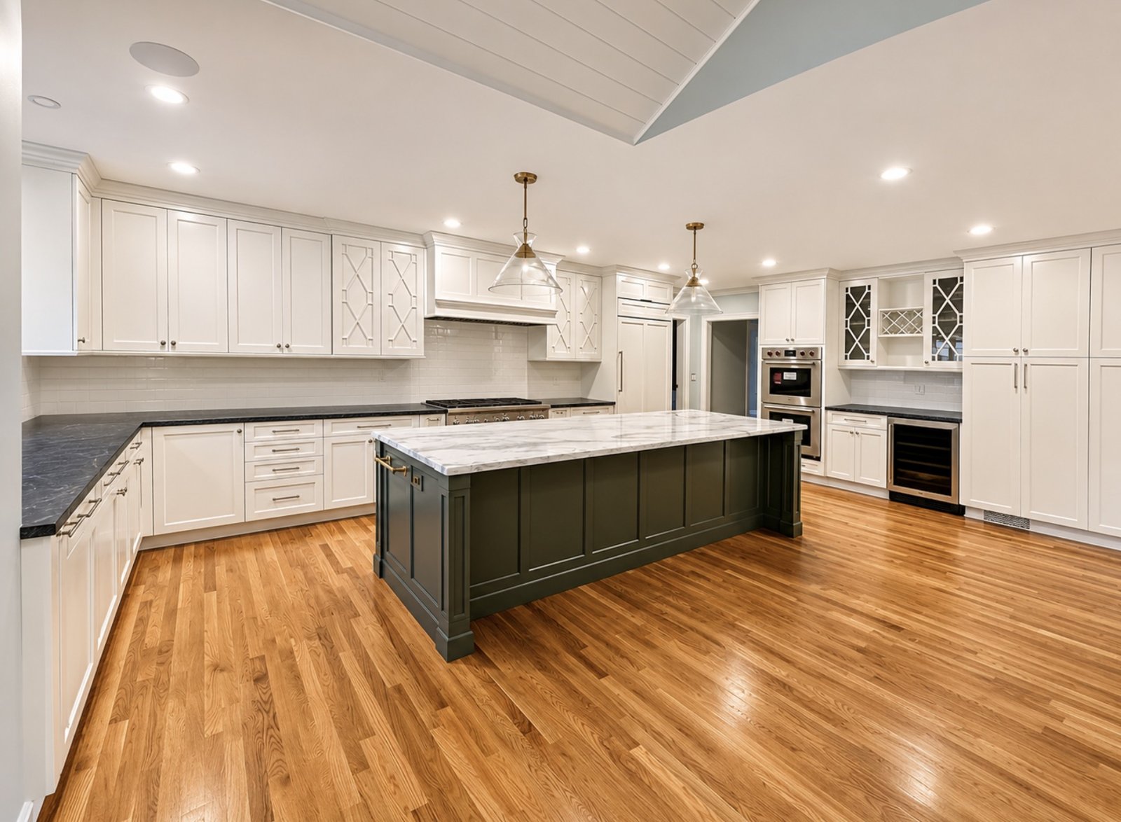 White kitchen with lattice-front cabinets, dark green island with marble top and oak floors