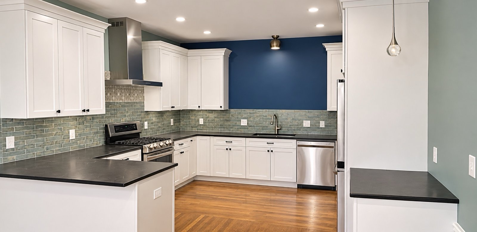 White shaker kitchen with sea-green tile backsplash and navy accent wall